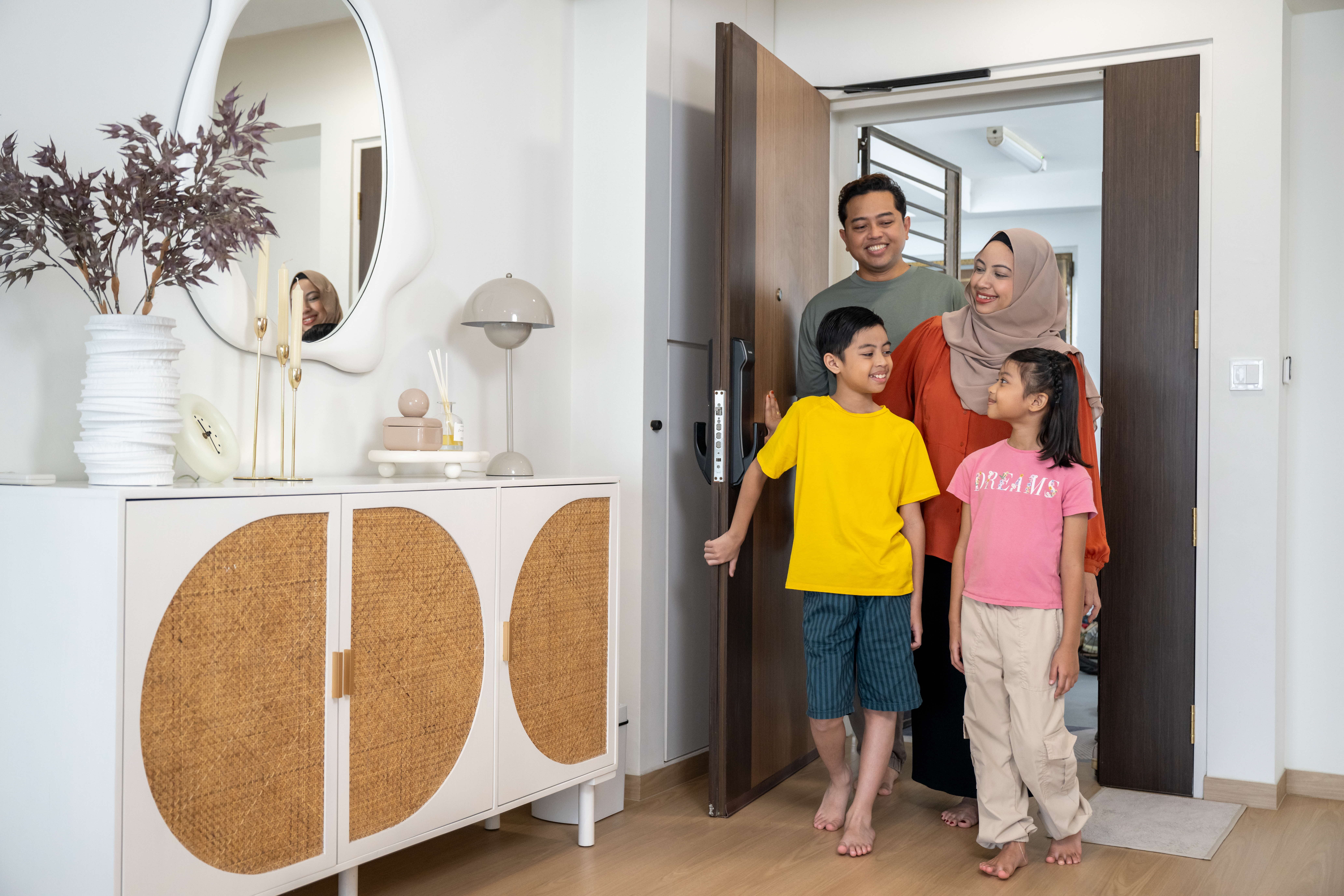 Parents and their two children entering their HDB flat